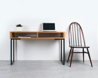 May include: A light wood desk with black metal legs and a shelf. A laptop computer is on the desk. A wooden chair with a slatted back is in the background.