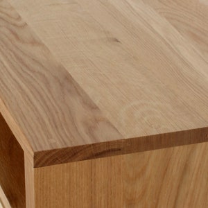 May include: Close-up of the top edge of a wooden table with a natural wood finish. The table has a simple, modern design with a smooth surface.