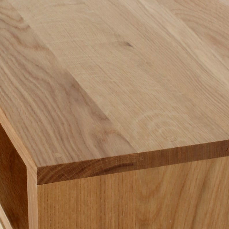 May include: Close-up of the top edge of a wooden table with a natural wood finish. The table has a simple, modern design with a smooth surface.
