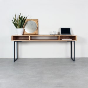 May include: A wooden desk with black metal legs and open shelves. A plant in a white pot, a round mirror, a laptop, and a mug are on the desk.