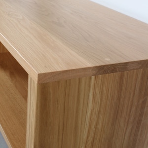 May include: A light-colored wooden console table or shelving unit featuring a smooth, flat top surface with a visible natural grain pattern. The piece has a rectangular edge and a side panel that extends downward, creating an open storage space.