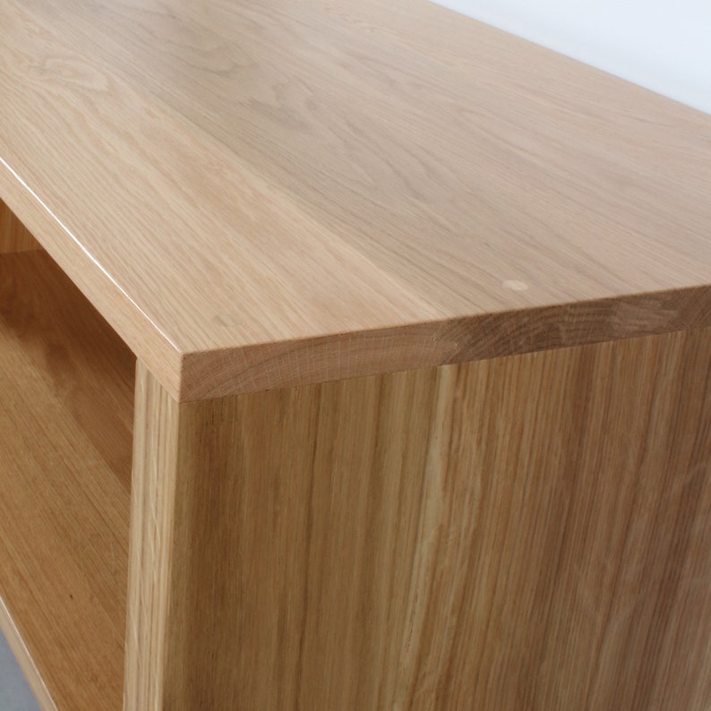 May include: A light-colored wooden console table or shelving unit featuring a smooth, flat top surface with a visible natural grain pattern. The piece has a rectangular edge and a side panel that extends downward, creating an open storage space.