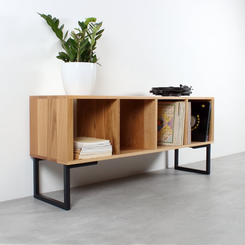 Puede incluir: Una estanter&iacute;a de madera con cuatro compartimentos, patas de metal negro y un tocadiscos en la parte superior. La estanter&iacute;a est&aacute; llena de libros y discos de vinilo.