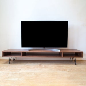May include: A dark brown wooden TV stand with a black TV on top. The stand has a shelf and two open compartments. The stand has hairpin legs.