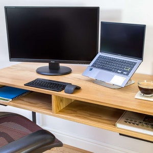 Könnte beinhalten: Ein heller Holzschreibtisch mit einem schwarzen Metallrahmen. Der Schreibtisch hat ein Regal darunter und einen Monitor, einen Laptop, eine Tastatur, eine Maus, eine Kaffeetasse und einen Stifthalter oben.