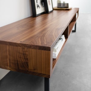 May include: A dark brown wooden entertainment console with black metal legs and open shelving. The console has a smooth, polished finish and is perfect for displaying books, plants, or other decorative items.