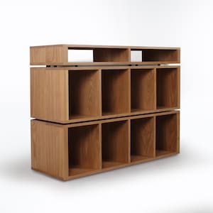May include: A wooden record shelf with two tiers of cubbyholes. The top tier has a shelf for displaying records. The shelf is made of light brown wood.