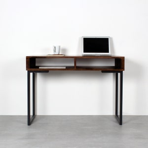 Könnte beinhalten: Ein dunkelbrauner Holzschreibtisch mit schwarzen Metallbeinen. Der Schreibtisch hat zwei Regale und einen Laptop auf dem oberen Regal.