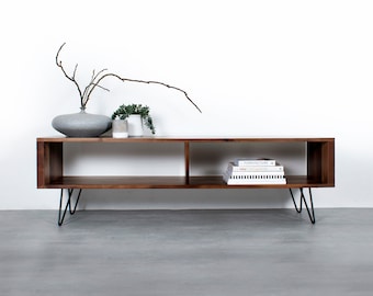 May include: A modern, rectangular wooden media console with two open compartments. The console is a warm brown color and has black hairpin legs. A gray vase with branches, small plants, and books are displayed on top.
