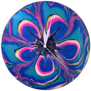 May include: A circular wall clock featuring a vibrant acrylic pour design with swirling patterns of bright blue, teal, magenta, and black. The clock face has a glossy finish and includes two simple white hands centered on the abstract floral-like motif.