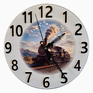 May include: A round wall clock with a white face and large black numerals. The center features a detailed image of a steam locomotive train traveling on tracks through a desert landscape with mountains under a cloudy sky at sunset.