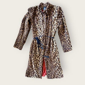 May include: A long-sleeved coat featuring a brown and black leopard print pattern. The coat has a high collar, a thin dark blue tie belt at the waist, and a visible red lining at the bottom opening. A small square label is visible at the neck.