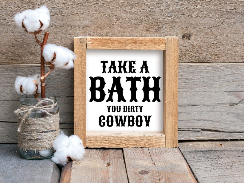Peut inclure: Un panneau en bois rustique avec le texte "TAKE A BATH YOU DIRTY COWBOY" en lettres noires. Un bocal en verre envelopp&eacute; de ficelle contient des tiges de coton. Le fond est en bois vieilli.
