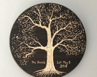 May include: A round wooden plaque with a woodburned design of a tree with branches and roots. The text "The Reeds Est May 5 2018" is inscribed on the plaque.