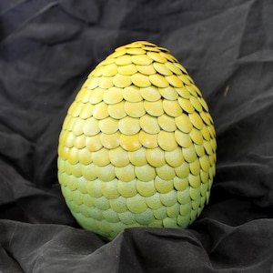 May include: A decorative egg-shaped object with a scale-like pattern. The egg transitions in color from a light green at the base to a yellow hue at the top. The object is set against a dark, textured background.