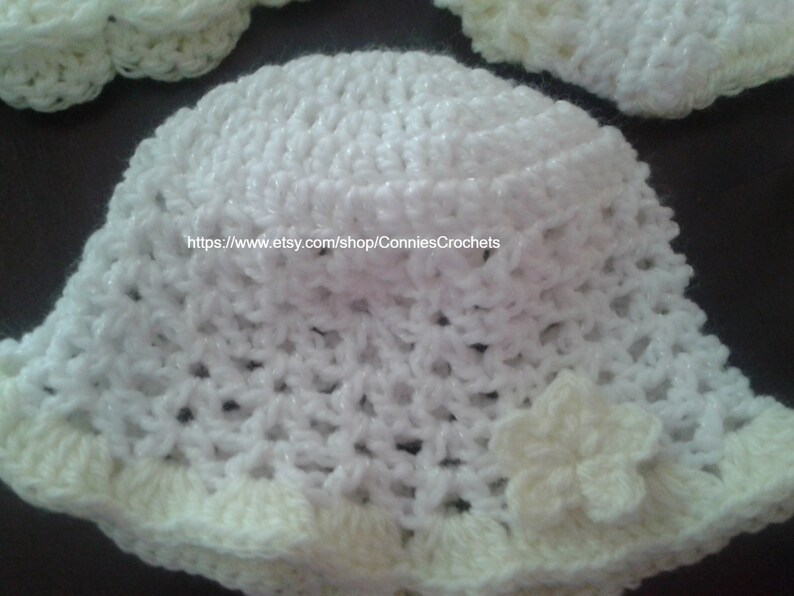 May include: White crocheted sun hat with a white flower accent. The hat has a wide brim and a crocheted band around the crown. The hat is made with a delicate, open stitch pattern. https://www.etsy.com/shop/ConniesCrochets
