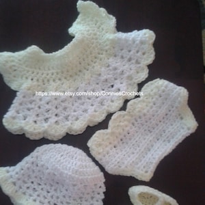 May include: A set of crocheted baby clothes in white and pale yellow. The set includes a hat, a top, and a pair of booties. The clothes are made with a delicate crochet stitch and have a scalloped edge.