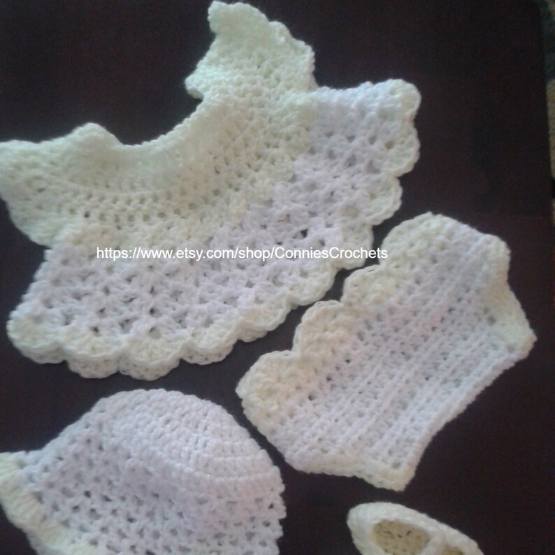 May include: A set of crocheted baby clothes in white and pale yellow. The set includes a hat, a top, and a pair of booties. The clothes are made with a delicate crochet stitch and have a scalloped edge.