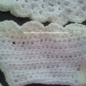 May include: White crocheted baby bonnet with a scalloped edge. The bonnet is made with a white yarn and has a cream colored trim.