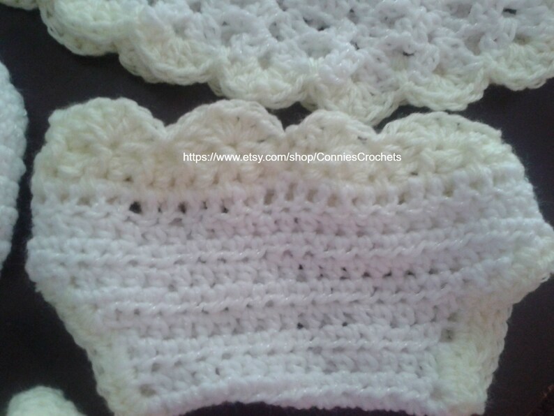 May include: White crocheted baby bonnet with a scalloped edge. The bonnet is made with a white yarn and has a cream colored trim.