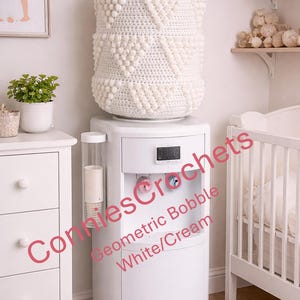May include: A white water cooler cover featuring a textured crochet pattern with raised bobble stitches arranged in geometric triangles. The cylindrical cover is designed to fit over a standard water jug, providing a decorative cream-colored finish.
