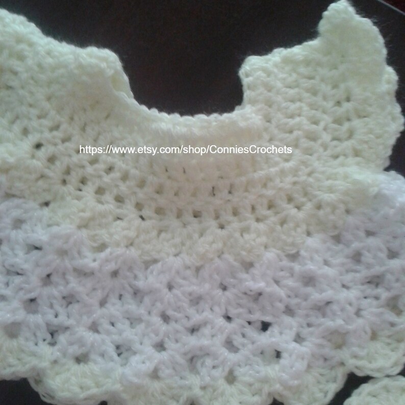 May include: A white crocheted collar with a scalloped edge. The collar is made with two different shades of white yarn, creating a subtle ombre effect. The text "https://www.etsy.com/shop/ConniesCrochets" is visible in the center of the collar.