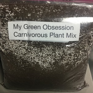 May include: A clear plastic bag filled with a dark brown and white granular mixture. A white label on the bag reads "My Green Obsession Carnivorous Plant Mix". The mix appears to be soil and perlite, suitable for carnivorous plants.