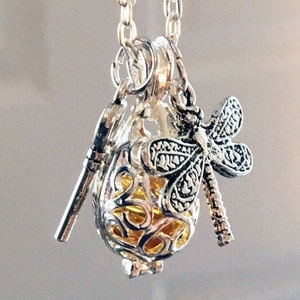 May include: Silver chain necklace with a silver and gold cage pendant featuring a dragonfly charm. The cage is open and has a small silver ball inside.