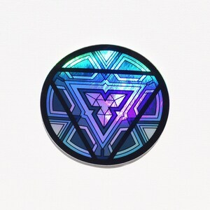 May include: A circular sticker with a geometric design. The design features a central triangle within a circle, with shades of blue, purple, and teal. The sticker has a black border and a holographic effect.