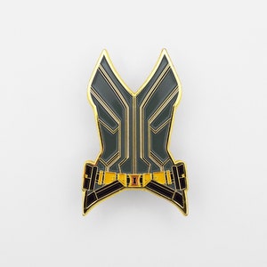 May include: A gold-colored pin with a black and gold design. The pin is shaped like a woman's torso and has a belt around the waist. The pin is a popular character from the Marvel Cinematic Universe.
