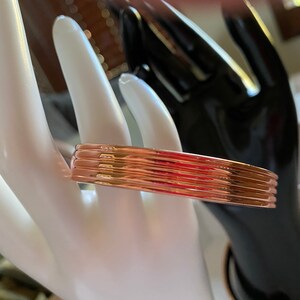 May include: A rose gold bangle bracelet with a ridged design. The bracelet is made of multiple thin bands of metal.