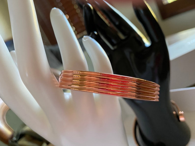May include: A rose gold bangle bracelet with a ridged design. The bracelet is made of multiple thin bands of metal.