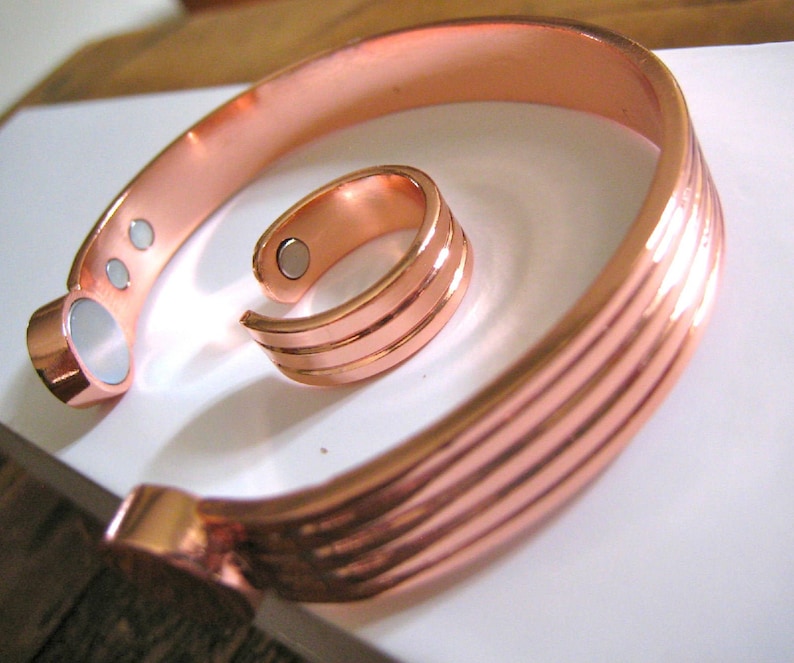 May include: A set of two copper bracelets with magnetic closures. The larger bracelet has a ridged design and the smaller bracelet is a ring.
