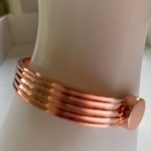 May include: A rose gold bangle bracelet with a ridged design and a smooth, rounded clasp.