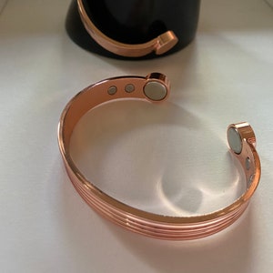 May include: A rose gold magnetic bracelet with a ridged design and multiple magnets.
