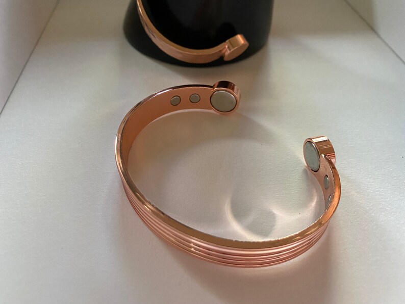 May include: A rose gold magnetic bracelet with a ridged design and multiple magnets.