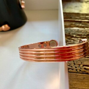 May include: A copper-colored magnetic bracelet with a ridged design. The bracelet has three magnetic closures.