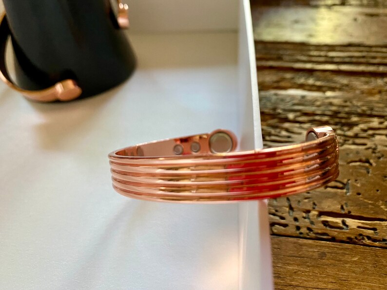 May include: A copper-colored magnetic bracelet with a ridged design. The bracelet has three magnetic closures.