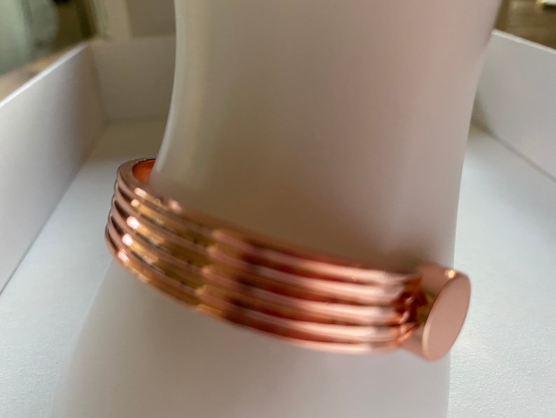 May include: A rose gold bangle bracelet with a ridged design and a smooth, rounded clasp.