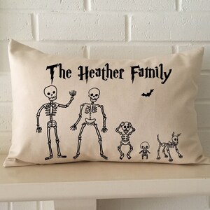 May include: A white throw pillow with black text that reads "The Heather Family". The pillow features a family of skeletons with a bat above them.