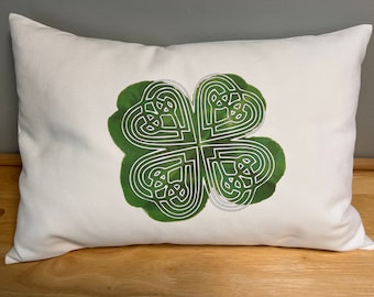 May include: White pillow with a green four-leaf clover design. The clover is outlined in white and has a Celtic knot pattern.