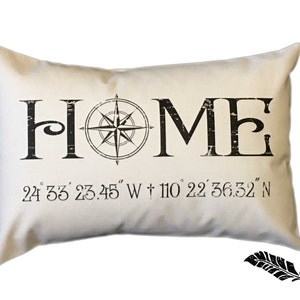 May include: A white pillow with black text that reads "HOME" and a compass graphic. The text below the word "HOME" reads "24 33' 23.45" W + 110 22' 36.32" N".