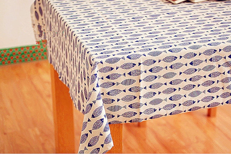 May include: A white tablecloth with a blue fish pattern. The tablecloth is draped over a wooden table.