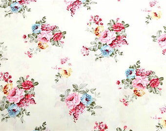 May include: A white fabric with a floral pattern featuring pink, blue, and yellow flowers. The flowers are arranged in clusters and are surrounded by green leaves.