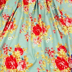 Puede incluir: Primer plano de una tela con estampado floral. La tela tiene un fondo azul claro con un patr&oacute;n repetido de rosas rojas, hojas amarillas y peque&ntilde;as flores azules y blancas. La tela est&aacute; doblada, creando sombras y profundidad.