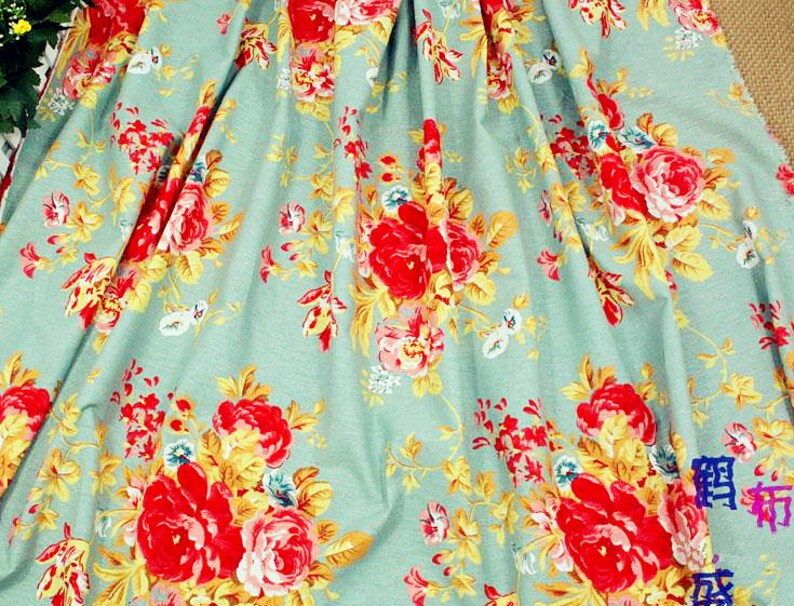 Puede incluir: Primer plano de una tela con estampado floral. La tela tiene un fondo azul claro con un patr&oacute;n repetido de rosas rojas, hojas amarillas y peque&ntilde;as flores azules y blancas. La tela est&aacute; doblada, creando sombras y profundidad.