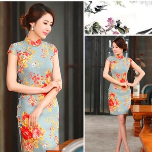 Puede incluir: Vestido azul claro de manga corta con cuello mandar&iacute;n y estampado floral. El vestido presenta flores rojas, amarillas y naranjas. El vestido tiene una silueta ajustada y llega a la rodilla.