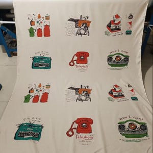May include: A white fabric with a repeating pattern of vintage-inspired illustrations. The illustrations include a typewriter, a rotary phone, a camera, and a sewing machine. The text "Quiet de Luxe", "Telephone", "Retro & Vintage", and "A 3010 Land Camera" is included in the design.