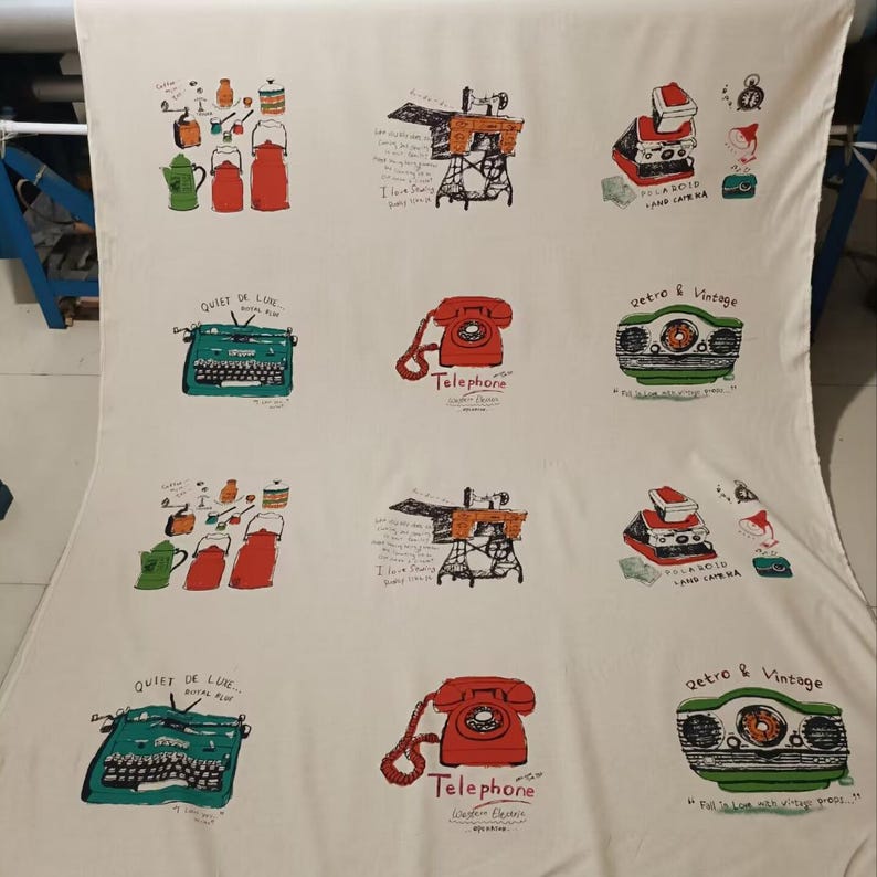 May include: A white fabric with a repeating pattern of vintage-inspired illustrations. The illustrations include a typewriter, a rotary phone, a camera, and a sewing machine. The text "Quiet de Luxe", "Telephone", "Retro & Vintage", and "A 3010 Land Camera" is included in the design.