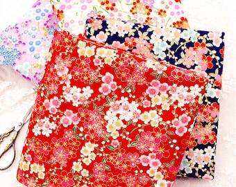 May include: A collection of floral patterned fabric in red, white, blue, and purple. The fabric features a repeating pattern of cherry blossoms and other flowers. A pair of gold scissors is visible on the left side.